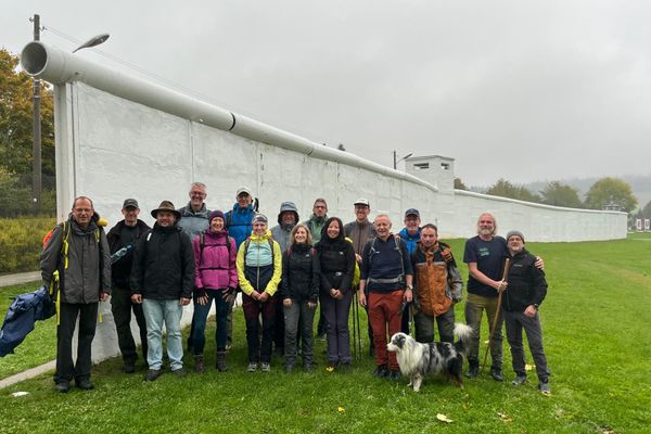 Eine Wandergruppe steht vor Resten der Mauer in Mödlareuth. Dort verlief die innerdeutsche Grenze