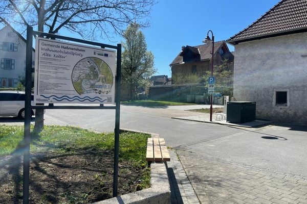 Hinweisschild mit Beschreibung zum Wohnmobilstellplatz Alter Kelter, nebenan befindet sich eine Sitzbank, im Hintergrund ist der Wohnmobilstellplatz