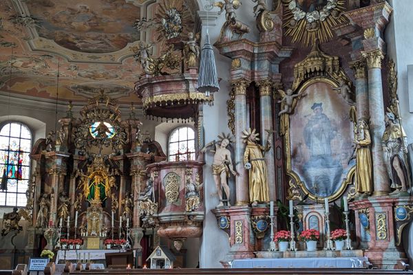Das Bild zeigt den Innenraum der Wallfahrtskirche Mariä Geburt in Glosberg. Man sieht Sitzbänke und prunkvolle Altäre, Gemälde und Statuen.