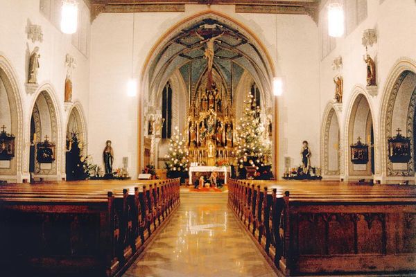 Kircheninnenraum mit Bankreihen und Seitenaltären. Unter dem Netzgewölbe steht ein eindrucksvoller Hauptaltar, flankiert von zwei Christbäumen.