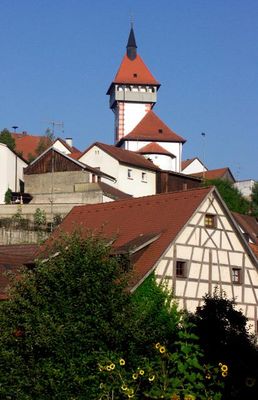 Mehrer Häuser in Hanglage vor dem aufragenden weißen Turm mit roten Spitzdach.