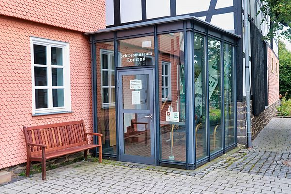 Eingangsbereich des Schlossmuseums. Im Winkel zwischen einem rosa verschindelten Gebäudeteil und einem Fachwerkteil ist ein Glasbau als Eingangsbereich eingebaut.