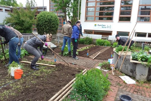 Menschen graben die Blumenbeete um und bereiten diese zur Bepflanzung vor.