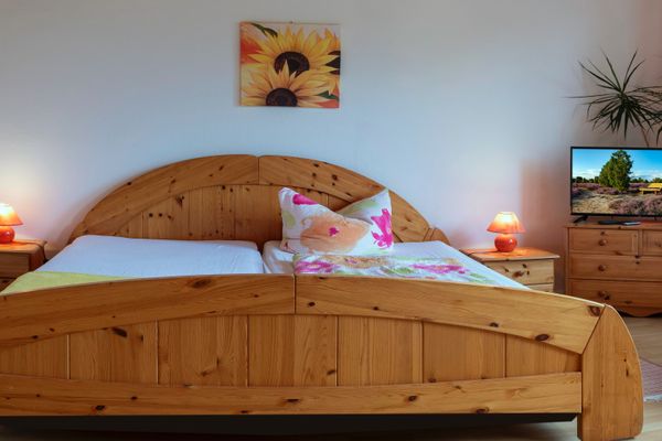 Doppelbett mit Holzrahmen, Nachttischen und Lampen, im Hintergrund ein Fernseher auf einer Kommode