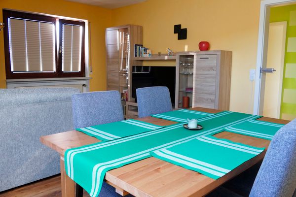 Wohnzimmer der Ferienwohnung Hirtenberg mit Esstisch im Vordergrund und Wohnwand im Hintergrund