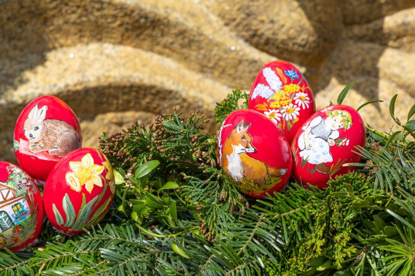 Sechs rote, bemalte Eier. Motive sind ein Fuchs, ein Hase, ein Blumenstrauß, eine Narzisse sowie ein Mädchen und ein Fachwerkhaus.