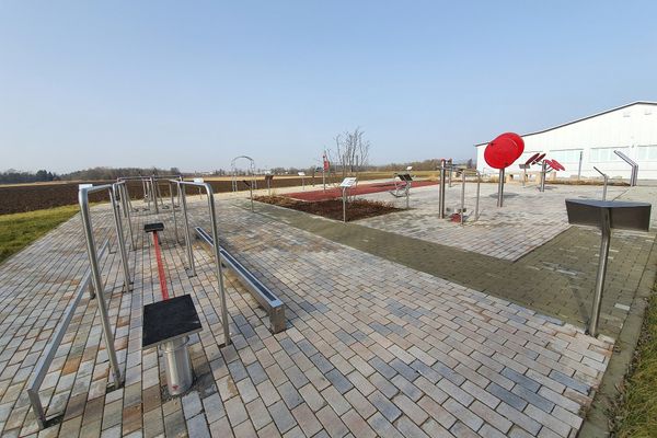 Bewegungspark mit verschiedenen Übungsstationen, dahinter ein Feld und daneben ein großes Gebäude.