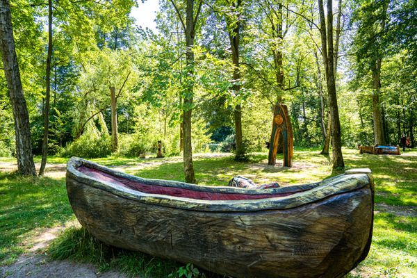 Das Bild zeigt einen Ausschnitt der Fantasiewelten in Mitwitz. Man sieht diverse Figuren aus Holz geschnitzt. Im Vordergrund sieht man ein Boot.