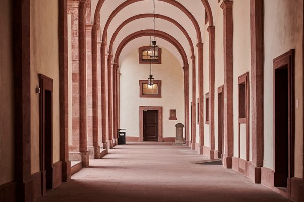 Langer Arkadengang mit hohen Rundbögen, rechteckigen Türen und Laternen an der Decke