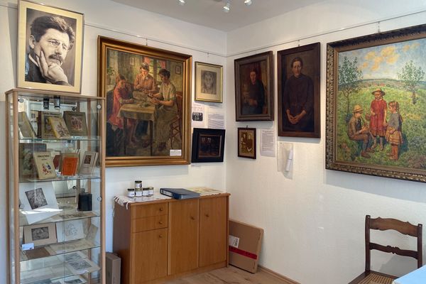 Ein gut ausgeleuchteter Raum mit Gemälden an den Wänden und Büchern sowie Radierungen und Zeichnungen in einer Vitrine ist zu sehen.