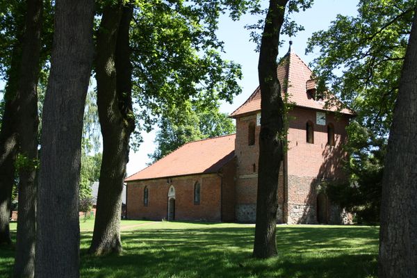 Blick auf die Kapelle St. Bartholomäus in Lüder mit Kirchturm, umgeben von großen Bäumen.
