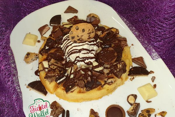 Auf dem Bild ist eine Waffel mit Schokolade und verschiedenen Schokoladen-Süßigkeiten zu sehen.