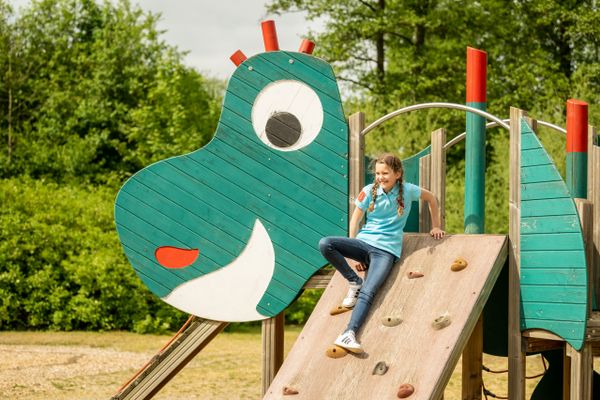 Ein Kind sitzt auf einer Kletterrampe der Drachenburg, die in den Körper des grünen Drachen geht
