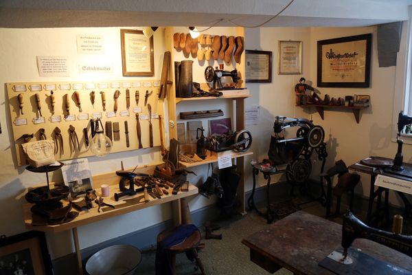 Blick in eine alte Schuhmacherwerkstatt An der Wand hängen Werkzeuge, Meisterbriefe und Leisten, davor stehen Maschinen.