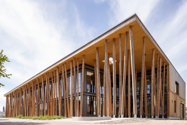 Außenansicht des Nawareums, die hauptsächlich die Naturbaumstämme, die die Fassade stützen, zeigt.