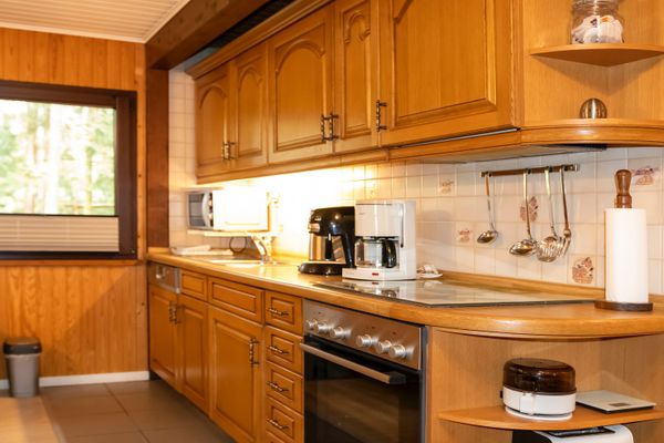Küchenzeile mit Holzschränken, Backofen, Kaffeemaschine und Mikrowelle neben einem Fenster.
