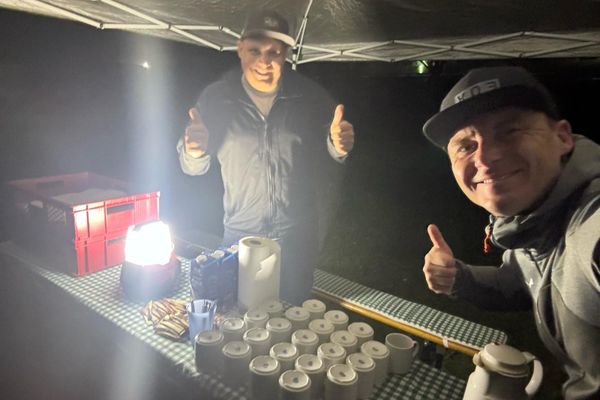 Das Bild zeigt zwei Personen, die in die Kamera lächeln. Es ist Nacht. Die zwei Personen sind Personal an einer Verpflegungsstation einer Nachtwanderung