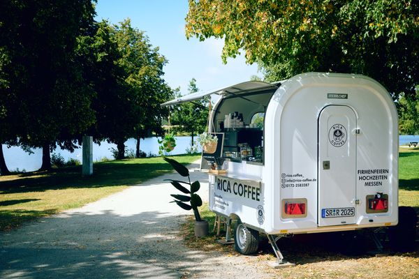 Auf dem Bild ist das mobile Café (der Anhänger) an einem See stehend zu sehen.