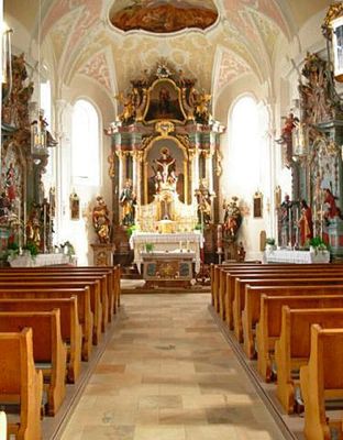 Kircheninnenraum mit Hauptaltar, zwei Seitenaltären, Gewölbedecke und Bankreihen.