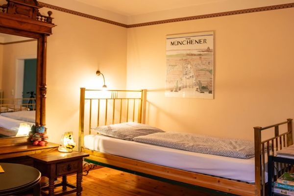 Einzelbett mit Bettwäsche neben einem Nachttisch mit Lampe, darüber ein Wandbild an der Wand.