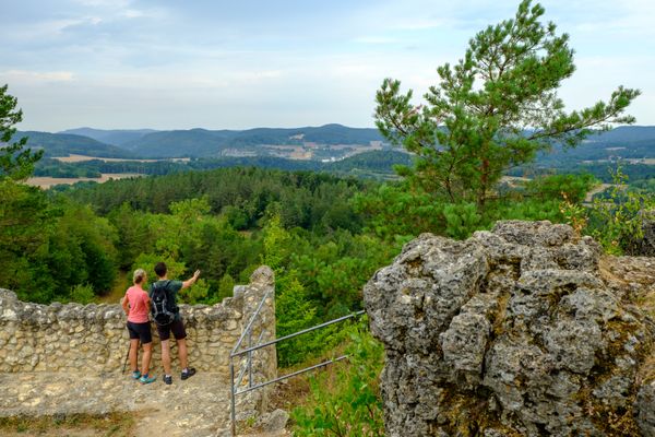 Ein Mann und eine Frau stehen an einem Aussichtspunkt und blicken in die Ferne. Sie stehen an einer alten steinernen Mauer.