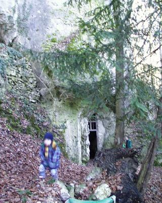 Eine Junge mit blauer Jacke und blauer Mütze läuft auf einem Waldweg vom Eingang der Höhle weg.