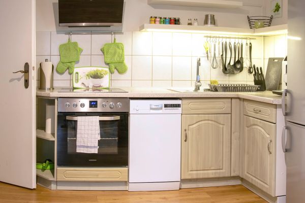 Küchenzeile mit Backofen, Spüle, Hängeschränken und aufgehängten Küchenutensilien an der Wand