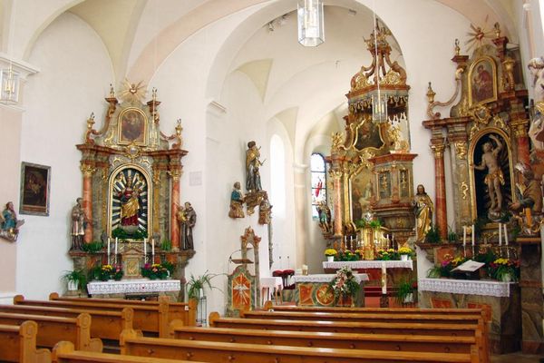 Kircheninnenraum mit Gewölbedecke, zentralem Hauptaltar, zwei Seitenaltären, Heiligenfiguren und Bankreihen.