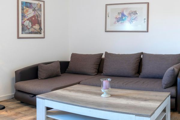 Sofa mit Kissen vor einem Couchtisch, daneben eine Stehlampe und Bilder an der Wand.