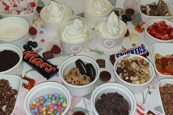 Auf dem Bild ist Frozen Yoghurt in Bechern zu sehen. Um die Becher herum sind verschiedene Dopings (ebenfalls in Bechern) zu sehen.