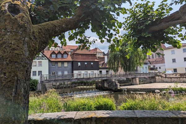 Das Bild zeigt die Jahnsalle in Kronach, hier sieht man die Altstadt Kronachs im Hintergrund. Das Foto wurde zwischen 2 Bäumen augenommen, diese sieht man in den Bildrändern.Direkt daneben fließt ein Fluss.