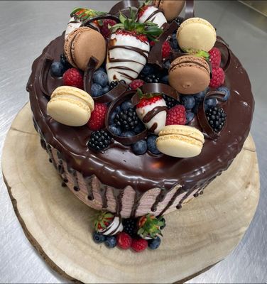 Auf dem Bild ist eine Torte mit Schokoguss zu sehen. Verziert ist die Torte mit verschiedenen Früchten, wie Erdbeeren, Himbeeren, Brombeeren und Heidelbeeren, sowie mit verschiedenen Macarons.