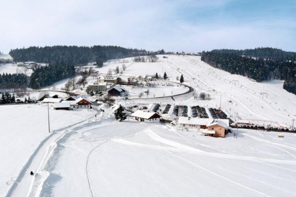 Ein Winterbild zeigt den verschneiten Ortsteil Grün. Im Vordergrund ein Wanderweg, im Hintergrund der Skilift Grün-Maibrunn. Schnee bedeckt Dächer, Wiesen und Wälder.