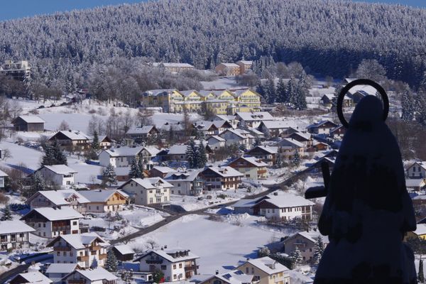 Rechts im Vordergrund steht die Statue des Steinernen Engelmars. Dahinter liegt ein Teil des winterlichen Sankt Englmar, überragt vom verschneiten Wald.