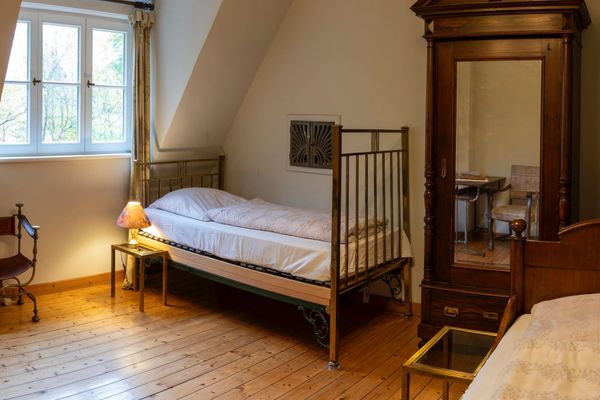Schlafzimmer mit zwei Einzelbetten, einem Nachttisch mit Lampe, Fenster und einem großen Kleiderschrank.