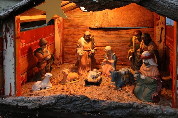 Eine weihnachtliche Krippe mit klassischen Krippenfiguren in einem kleinen Holzhaus. Der Innenraum ist ausgeleuchtet am Giebel hängt ein goldener Stern.