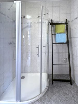 Geflieste Dusche mit gebogener Glasabtrennung und danebenstehendem Handtuchhalter mit zwei Handtüchern.