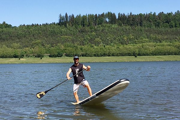 Mann stehend mit Paddel auf einem langen Board auf dem Wasser