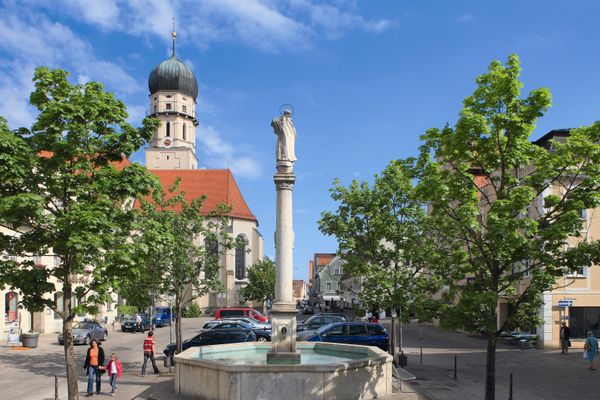 Der Betrachter sieht auf den prächtigen Marienbrunnen mit einer Madonna auf der mittigen Säule und dahinter die Stadtpfarrkirche.