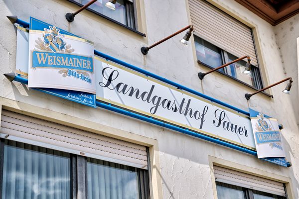 Blick auf ein blau-weißes  Schild mit Aufschrift Landgasthof Sauer.