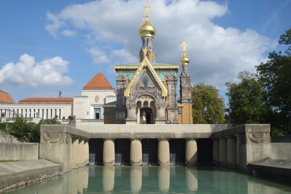 Russisch-orthodoxe Kapelle mit goldenen Zwiebeltürmen hinter einer Brücke über einem Wasserbecken