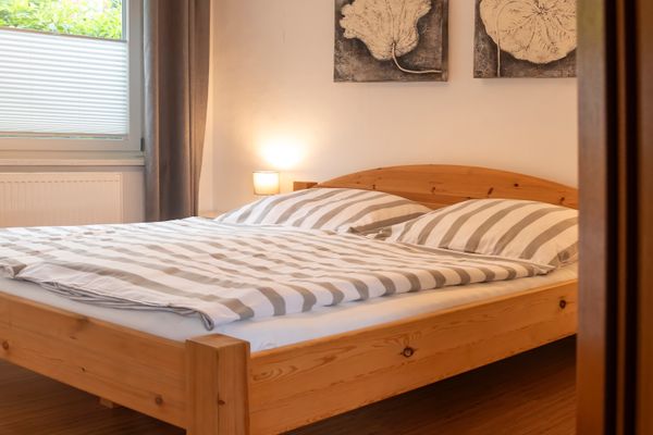 Doppelbett mit gestreifter Bettwäsche, Holzrahmen und Nachttischlampe neben einem Fenster.
