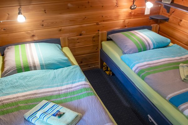 Zwei Einzelbetten mit gemusterter Bettwäsche stehen parallel in einem Raum mit Holzverkleidung und Wandlampen.