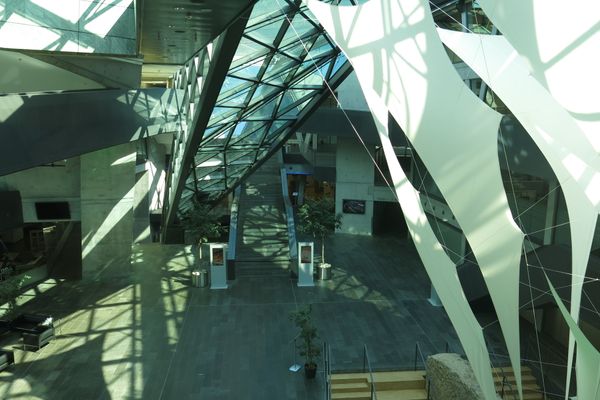 Blick in das Atrium eines modernen Gebäudes mit Glasdach, Treppe und großen weißen Säulen mit schwarzen Linien.