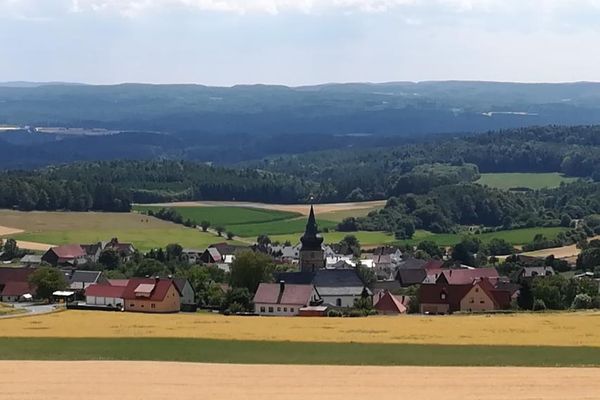 Blick in die Ferne auf hügeligen Felder und Wälder. Mittig ein Dorf mit einer Kirche.
