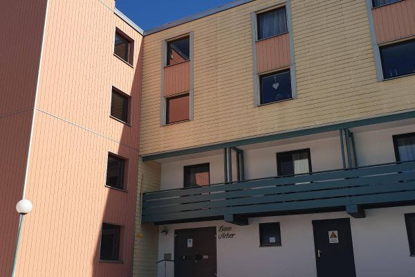 "Haus Arber" steht über dem Eingang zur Apartmentanlage, darüber befindet sich ein langgezogener, grüner Balkon. Die in zwei Farben vertäfelten Wände sind mit mehreren viereckigen Fenstern versehen.