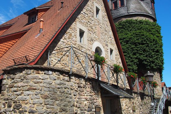 In einem Raum mit weißem Putz stehen alte Töpfereigegenstände. Im Vordergrund ist eine hölzerne Drehscheibe zu sehen, unten eine große und oben eine kleinere, kreisrunde Holzscheibe, die verbunden sind mit einer Metallstange. Daneben steht auf dem Boden ein weißer Würfel, auf dem Metallzangen und andere Hilfsmittel liegen. Dahinter ist eine Holzbank, auf der sich irdene Gefäße und Tonrohmasse befinden. An der Wand dahinter ist ein Holzregal mit verschiedenen bemalten Tongefäßen, worüber ein großes hölzernes Schild mit der Aufschrift "Töpferei von Heinrich Seitz" hängt. Links neben diesem Arrangement steht eine Metallmaschine, die scheinbar für das Formen von Tonblumentöpfen vorgesehen ist.
