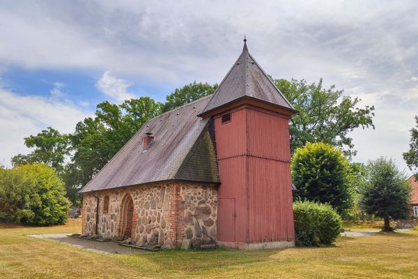 Feldsteinkapelle in Dalldorf im Landkreis Uelzen mit rotem hölzernem Glockenturm, schiefergedecktem Dach und Rasenfläche im Vordergrund unter sommerlichem Himmel, Lüneburger Heide