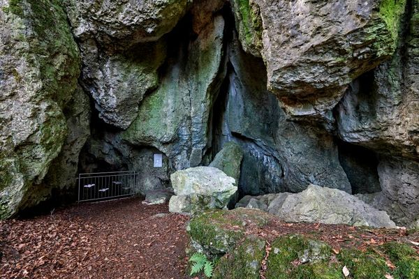 In einer massiven Felswand ist ein Metallgeländer vor dem Zugang zur Höhle angebracht.