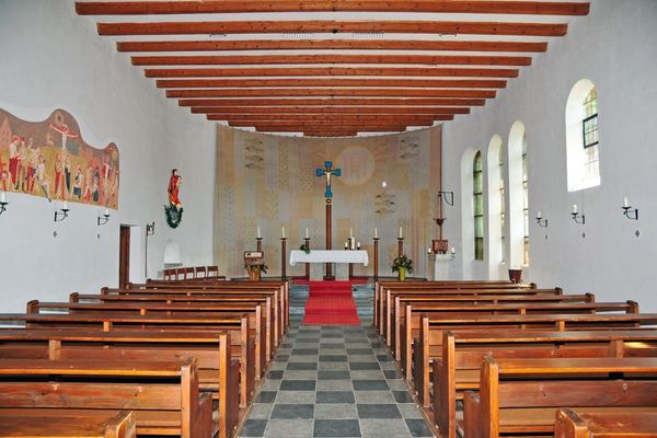 Innenraum der Kirche St. Wolfgang in Rettenbach mit einem deckenhohen, gewölbten Wandteppich hinter dem Altar, auf dem unter anderem einige Fische dargestellt sind.
